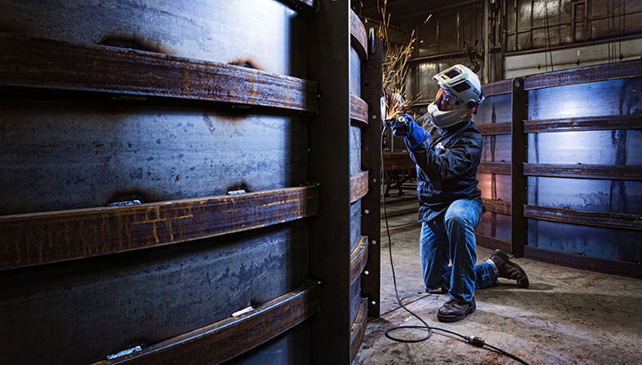 Operator grinding on large structure, wearing a welding helmet with a grind shield 