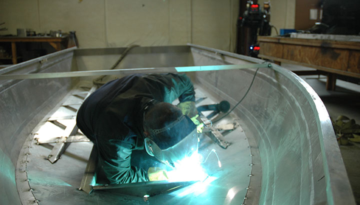 An operator welds an aluminum boat hull