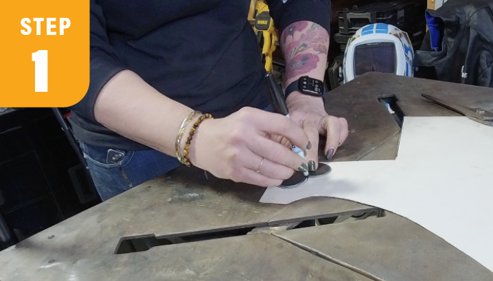 Person tracing a pattern onto a sheet of material at a workbench